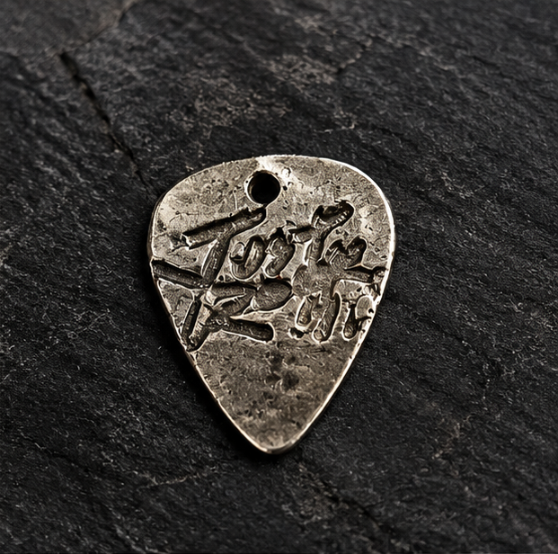 Engraved teardrop-shaped fine silver guitar pick on a black background
