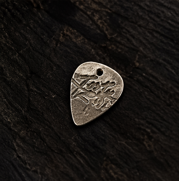 Hand holding an engraved fine silver guitar pick against guitar strings